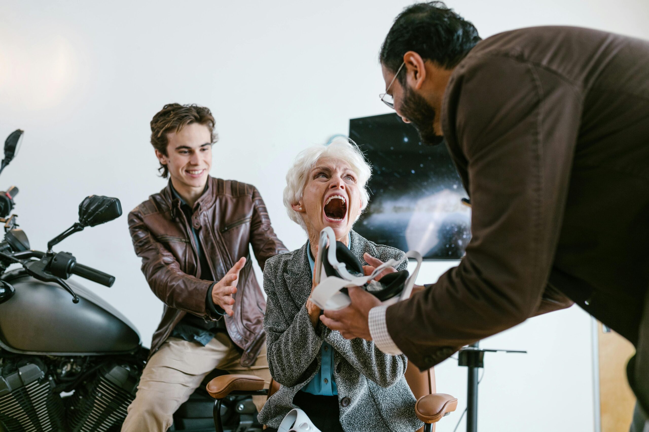 An excited senior woman experiencing virtual reality with the help of two young men indoors.